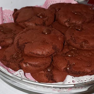 May include: A close-up of a plate of chocolate chip cookies. The cookies are dark brown and have a soft, chewy texture. They are arranged in a circle on a white doily.