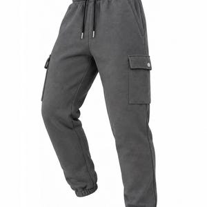 May include: Dark charcoal grey sweatpants featuring an elastic waistband with black drawstring cords, side pockets, and large cargo pockets on each thigh with button closures. The trousers have ribbed elastic cuffs at the ankles for a secure fit.
