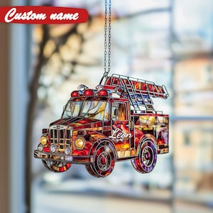 Puede incluir: Adorno de camión de bomberos de vidrieras con una escalera, sirenas y el nombre "Leon". El adorno es principalmente rojo con detalles en amarillo y naranja. Cuelga de una cadena plateada.