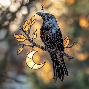 Könnte beinhalten: Glasmalerei-Rabe auf einem Ast mit Blättern und einem Halbmond. Der Rabe ist schwarz mit einem detaillierten, strukturierten Design. Die Blätter und der Mond sind bernsteinfarben und bilden einen auffälligen Kontrast. Ein dekoratives Stück.