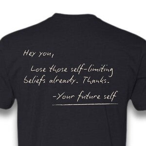 May include: Black t-shirt with white text that reads "Hey you, Lose those self-limiting beliefs already. Thanks. -Your future self"