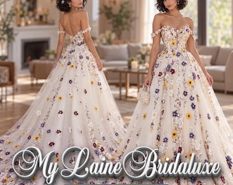 May include: An off-the-shoulder floor-length gown featuring a white base with colorful floral embroidery in yellow, purple, and maroon. The dress has a sweetheart neckline and a full skirt. Text reads: My Laine Bridaluxe Designed for Your Happily Ever After.