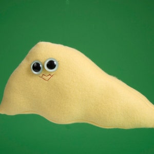 May include: A yellow, bean-shaped soft toy with googly eyes and a stitched smile, set against a green background. The toy has a whimsical design, and is made of a soft material. The toy is designed to be cuddled.