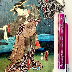 Könnte beinhalten: Ein japanischer Holzschnitt aus der Zeit mit einer Frau in einem Kimono, einer silbernen Kettenkette und einem rosa Stift mit silberner Kappe und einem floralen Design.