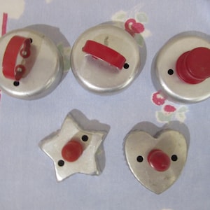 May include: A set of five metal cookie cutters with red handles. Three cutters are circular with varying handle styles, one is star-shaped, and one is heart-shaped. Each cutter features a small hole near the handle for air release.