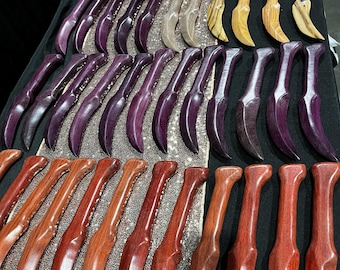 May include: A collection of numerous curved wooden handles arranged in rows. The handles feature various natural wood grain patterns and are finished in shades of deep red, vibrant purple, light tan, and dark brown, all with a smooth, polished surface.