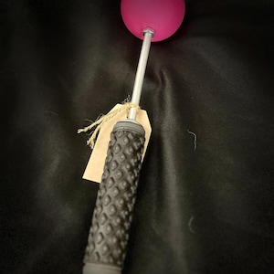 May include: A pink ball on a long silver handle with a black textured grip. The handle has a brown paper tag attached to it.