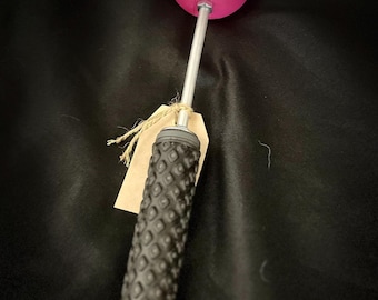 May include: A pink ball on a long silver handle with a black textured grip. The handle has a brown paper tag attached to it.