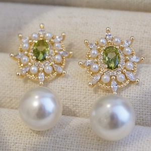 May include: A pair of gold earrings with a green gemstone and a pearl drop. The earrings feature a delicate floral design with small white stones.