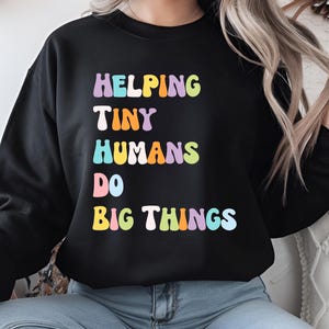 May include: Black sweatshirt with the text "Helping Tiny Humans Do Big Things" in rainbow colours.