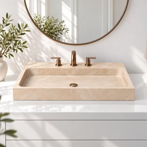 Peut inclure: Un lavabo rectangulaire en pierre beige avec une finition lisse et une bonde centrale. Il présente un rebord en pierre assorti avec une robinetterie à trois trous en bronze brossé, incluant deux poignées et un bec central.