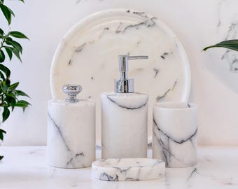 May include: A marble bathroom set featuring a soap dispenser, a tumbler, a jar with a lid, and a soap dish. The set is white with gray veining and chrome accents. A matching marble tray is in the background.