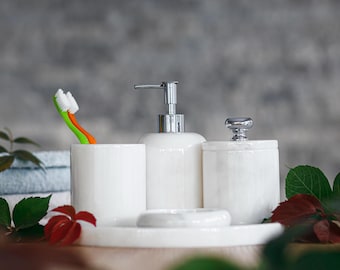 May include: White marble bathroom accessories set with a soap dispenser, toothbrush holder, and cotton swab container. The set is on a white marble tray.
