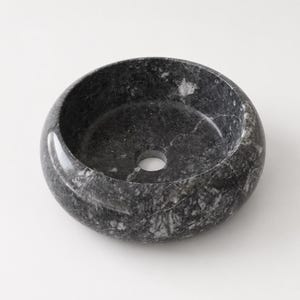 May include: A round vessel sink crafted from dark gray and black marble with prominent white veining throughout the stone. The basin features a smooth, polished finish and a centered circular drain hole at the bottom of the bowl interior.