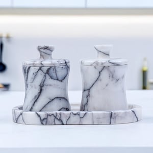 May include: A marble kitchen set featuring two lidded jars and a matching tray. The jars and tray are white with gray veining. The jars have a curved shape and a small handle on top. The set is displayed on a white surface.