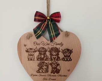 Può includere: Una targa in legno a forma di cuore appesa a uno spago di iuta, sormontata da un nastro a quadri rosso e verde. La targa presenta il testo inciso Our Wee Family, illustrazioni di sei mucche Highland e i nomi Dylan, Stuart, Michelle, Matthew, Ella e Daniel.