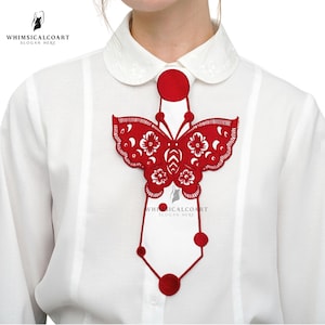 May include: A red butterfly-shaped brooch with floral cutouts is displayed on a white collared shirt. The brooch has a geometric design with circular accents and the text "WHIMSICALCOART" and "SLOGAN HERE".