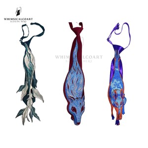 Puede incluir: Tres corbatas bordadas con diseños únicos. Una corbata presenta un patrón de hojas verde oscuro y plateado, otra tiene una base roja con un diseño azul en forma de llama, y la tercera tiene una base morada con un diseño de animal azul y naranja. Las corbatas se muestran sobre un fondo blanco.