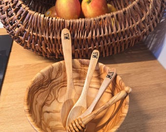 May include: Four wooden spoons in a wooden bowl. The spoons are all different sizes and have a natural wood finish. The bowl is made of olive wood and has a beautiful grain pattern.