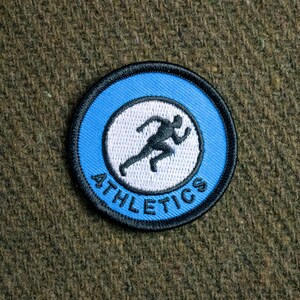 Peut inclure: Un patch circulaire bleu et blanc avec une silhouette de coureur et le texte "ATHLETICS" autour du bord.