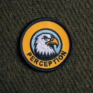 May include: A yellow and black embroidered patch featuring a white bald eagle head and the word "PERCEPTION" in black.