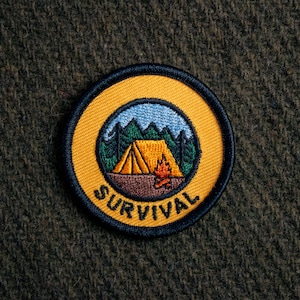May include: A yellow embroidered patch with a tent, campfire, and trees inside a circle. The text "SURVIVAL" is written around the circle.