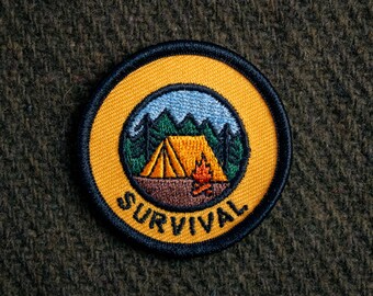 May include: A yellow embroidered patch with a tent, campfire, and trees inside a circle. The text "SURVIVAL" is written around the circle.