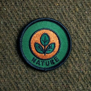 May include: A green and orange embroidered patch with the word "NATURE" and a stylized green leaf design.