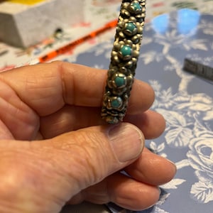 May include: Silver-toned bracelet with turquoise-colored stones set in a floral design. The bracelet is made of metal and features a series of flower-shaped links, each holding a small, round turquoise stone. The bracelet is a piece of jewelry.