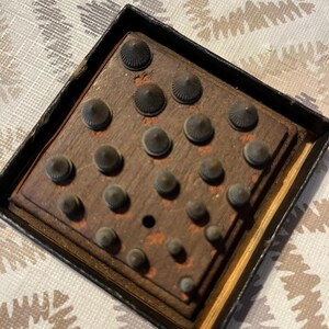 May include: A vintage wooden box with a dark finish, containing a set of small, cone-shaped metal tools. The tools are arranged on a wooden base, with a variety of sizes. The box has a black frame.