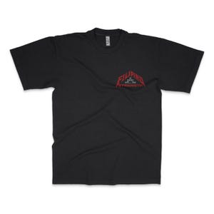 May include: Black t-shirt with a crew neck and short sleeves. The shirt features a red graphic on the upper left chest that reads "FILIPINO STRENGTH" in a stylized font. The graphic includes a crown design.