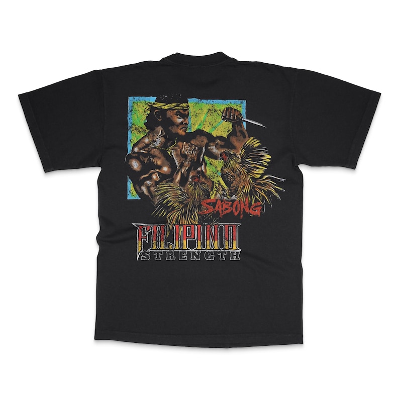 May include: Black t-shirt featuring a graphic of a muscular figure holding a knife, with the text "SABONG" and "FILIPINO STRENGTH" in a vintage style. The design includes a blue and green background.