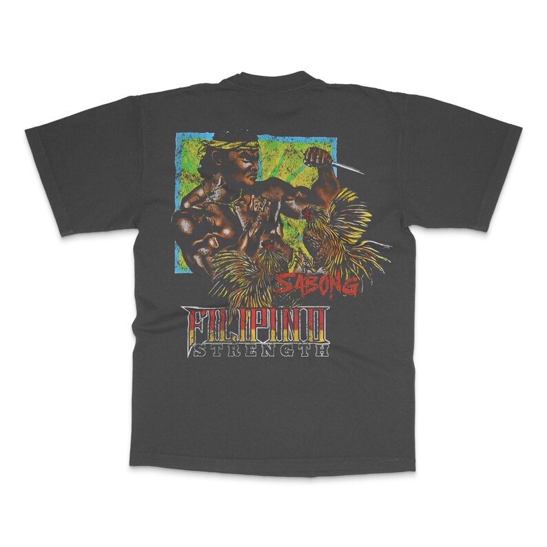 May include: Dark gray t-shirt featuring a graphic of two muscular figures in combat, with a knife. The design includes the text "SABONG" and "FILIPINO STRENGTH" in a vintage style, with a blue, green, and yellow background.
