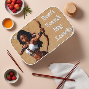 Op de afbeelding: Een witte lunchbox met een bruin houtnerfmotief. De lunchbox heeft een afbeelding van een vrouw met een bruine huid en lang zwart haar, die een boog en pijl vasthoudt. De tekst "Don't Touch My Lunch" staat op de lunchbox.