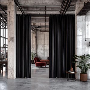 May include: A modern office space with a concrete ceiling and walls. Black curtains are used as room dividers. A red armchair and a couch are visible in the background.