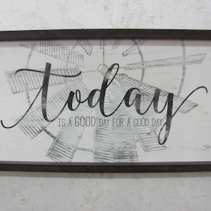 May include: A framed wood sign with a white background and black text that reads "Today is a good day for a good day". The sign features a black and white image of a windmill.