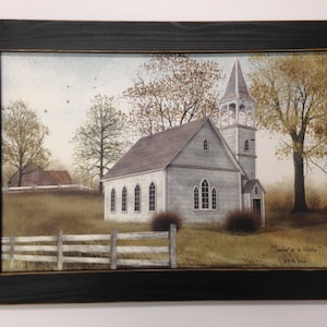 May include: A framed painting of a white church with a steeple, surrounded by trees and a wooden fence. The painting is in a rustic style and has a light blue sky in the background. The text "Sunlit up to Heaven" is written in the bottom right corner.