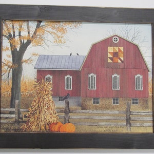 May include: A painting of a red barn with a patchwork quilt design on the side. The barn is surrounded by a wooden fence and there are corn stalks and pumpkins in the foreground. The painting is framed in a black frame.