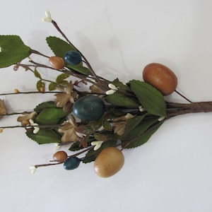 May include: A bouquet of artificial greenery with brown, blue, and cream colored eggs. The stems are wrapped in brown paper.