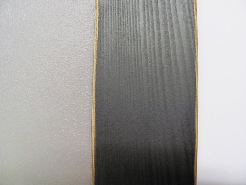 May include: A close-up of a vertical wood panel with a black stain and a gold-coloured border. The wood grain is visible.