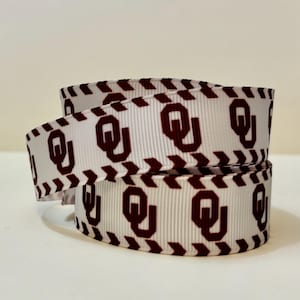 May include: White ribbon with a repeating maroon "OU" logo pattern. The edges are lined with a maroon chevron design. The ribbon is coiled, showcasing the design and texture.
