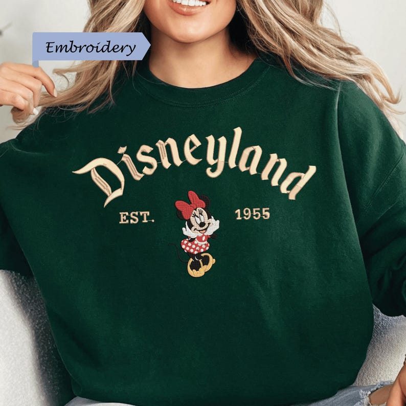 A woman wearing a green sweater with the word "Disneyland" and the year "1955" printed on it.