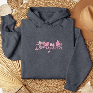 A gray hoodie with the text "Disneyworld" printed on it, along with various Disney-themed graphics, is laid out on a woven mat.