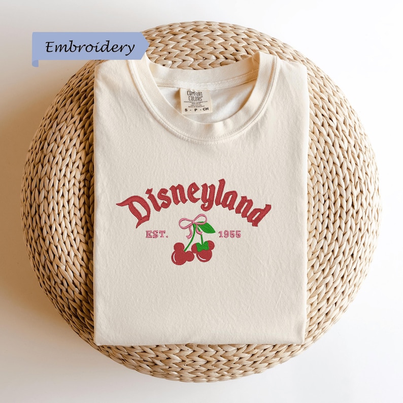 A white t-shirt with a Disneyland logo and text, laid out on a woven basket.