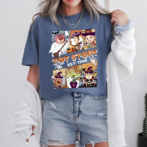 May include: A blue t-shirt with a Halloween-themed graphic of Toy Story characters. The design includes images of Lotso, Woody, and other characters in Halloween costumes, with the text "TOY STORY EST. 1995".
