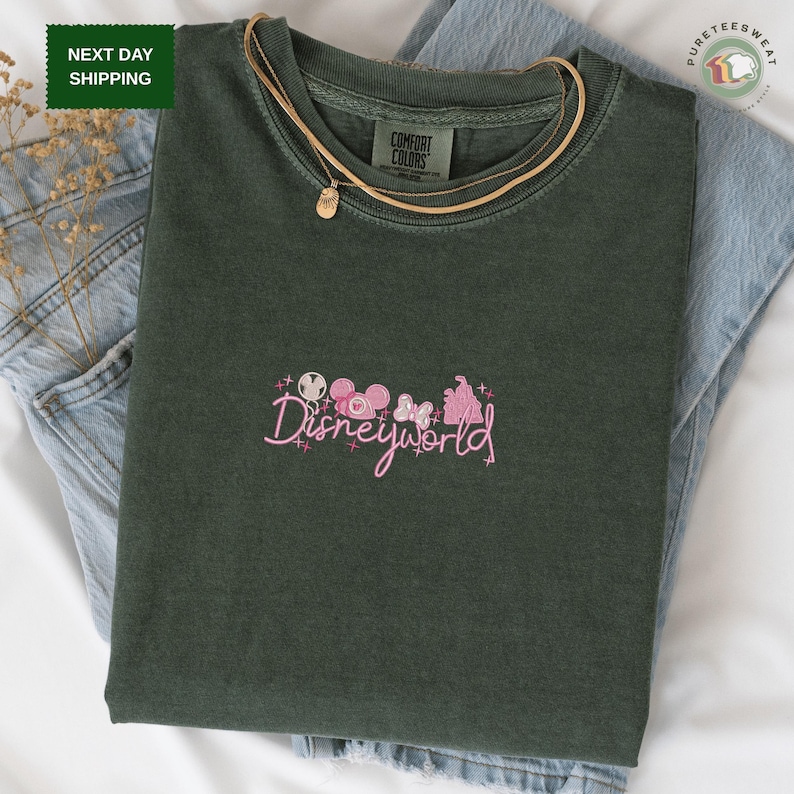 a green t-shirt with a pink Disneyworld logo printed on it, along with a pair of blue jeans.