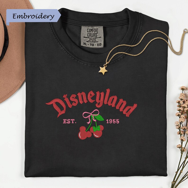 a black t-shirt with a Disneyland logo and text, along with a necklace and some flowers.