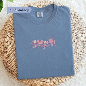 A blue t-shirt with a Disney World logo embroidered on it, placed on a woven basket.