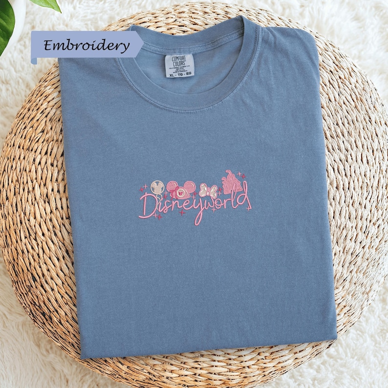 A blue t-shirt with a Disney World logo embroidered on it, placed on a woven basket.