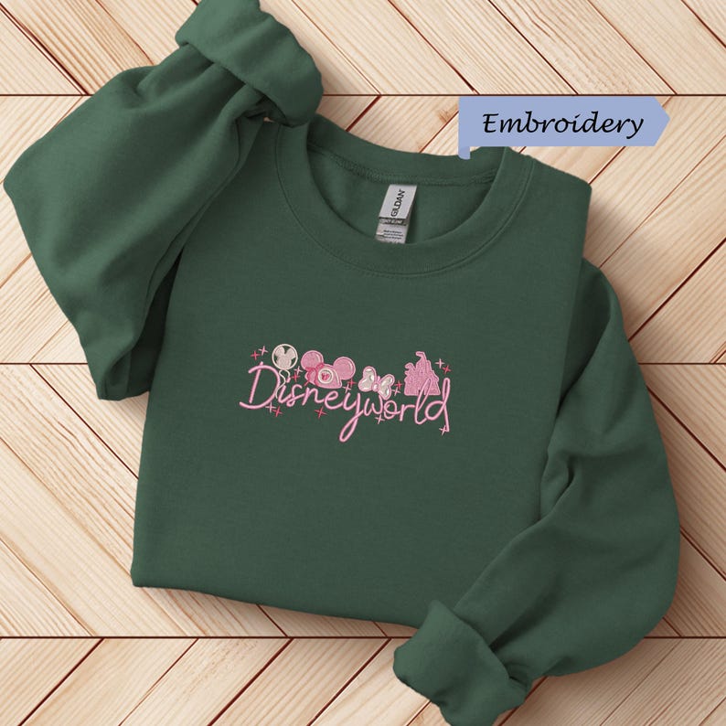 A green sweater with the Disneyworld logo printed on it, laid out on a wooden surface.